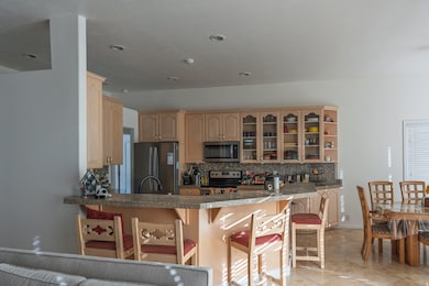 Kitchen with light brown cabinetry, a breakfast bar, backsplash, appliances with stainless steel finishes, and a peninsula