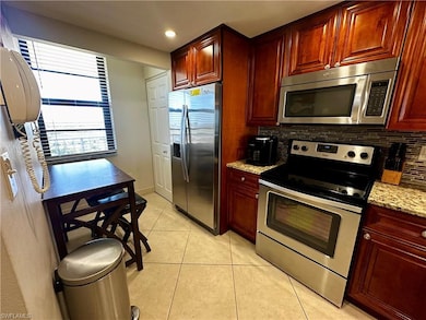 Kitchen featuring stainless steel appliances, light stone counters, decorative backsplash, light tile patterned flooring, and reddish brown cabinets