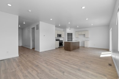 Kitchen with open floor plan, light countertops, appliances with stainless steel finishes, a center island with sink, and light wood-style floors
