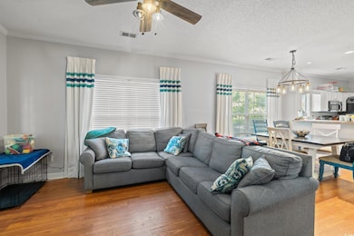 Living room featuring light wood-type flooring, ceiling fan, ornamental molding, a textured ceiling, and a chandelier