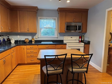 Kitchen with stainless steel microwave, light wood-style floors, electric stove, and brown cabinetry