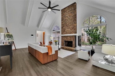 Living room featuring dark wood-style floors, beamed ceiling, a fireplace, high vaulted ceiling, and ceiling fan