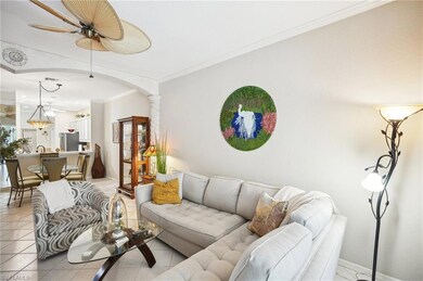 Living room featuring ornate columns, light tile patterned flooring, crown molding, and ceiling fan