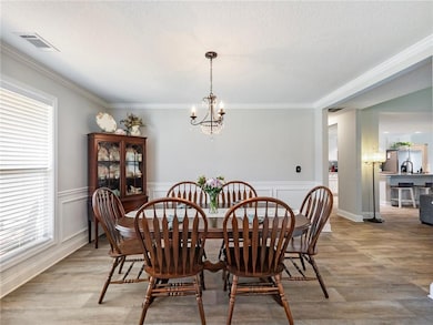 Dining area featuring a chandelier, crown molding, light wood finished floors, wainscoting, and a textured ceiling