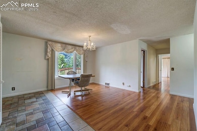 Unfurnished dining area featuring a chandelier, a textured ceiling, wood finished floors, and baseboards