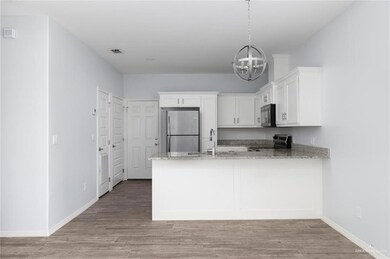 Kitchen with light stone counters, freestanding refrigerator, a peninsula, white cabinets, and electric stove