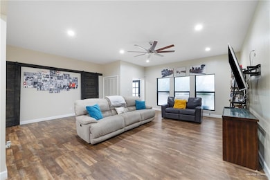 Living room with a barn door, wood finished floors, recessed lighting, and a ceiling fan