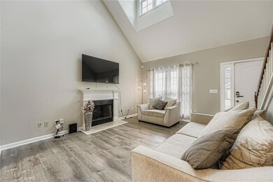 Living area with high vaulted ceiling, a skylight, a fireplace with raised hearth, wood finished floors, and stairs