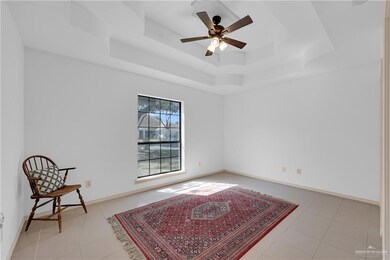 Living area with light tile patterned floors, ceiling fan, a tray ceiling, and baseboards
