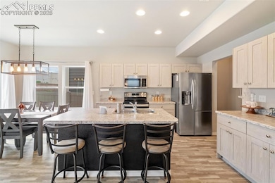 Kitchen with appliances with stainless steel finishes, a kitchen island with sink, light wood-type flooring, a breakfast bar area, and light stone counters