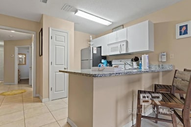 Kitchen featuring a peninsula, light tile patterned floors, light stone counters, white cabinets, and white appliances