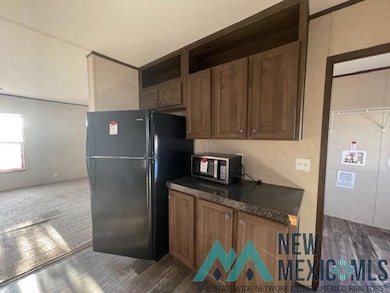 Kitchen with freestanding refrigerator, open shelves, brown cabinets, dark wood-style floors, and stainless steel microwave