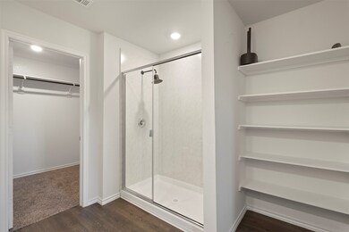 Full bathroom featuring a shower stall, dark wood-type flooring, and a spacious walk-in closet
