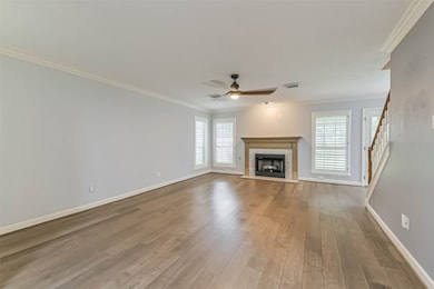 elcoming entryway leading into a spacious living area with hardwood floors and a fireplace. The room is bright, featuring large windows with shutters, and there's a staircase visible on the right. The neutral color palette and crown molding add a touch of elegance.