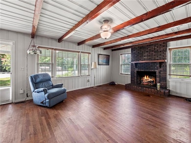 Unfurnished room with wood finished floors, a fireplace, beam ceiling, wood walls, and a ceiling fan