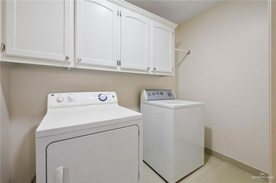 Clothes washing area with cabinet space, washing machine and dryer, baseboards, and light tile patterned flooring