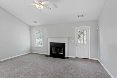 Unfurnished living room featuring ceiling fan, a textured ceiling, a fireplace with flush hearth, and carpet floors