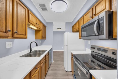 Kitchen featuring stainless steel appliances, light wood-style flooring, brown cabinets, and light stone countertops