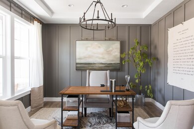 Office space with a chandelier, wood finished floors, a tray ceiling, and a decorative wall