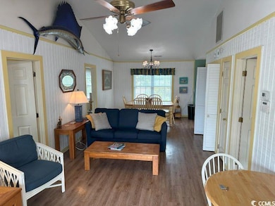 Living room with lofted ceiling, ceiling fan with notable chandelier, and hardwood / wood-style floors