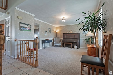 Carpeted living room with wallpapered walls, ornamental molding, and tile patterned floors