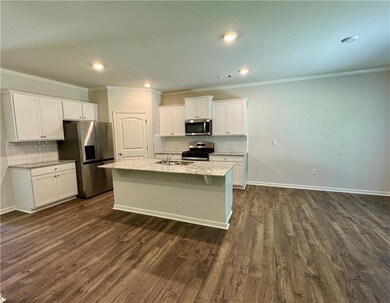 Kitchen with crown molding, decorative backsplash, white cabinetry, stainless steel appliances, and a center island with sink