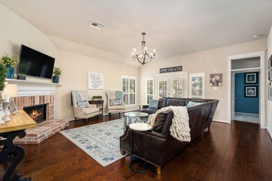 Spacious living room overlooks the wooded park in the back of the home, and features plantation shutters and a brick fireplace.