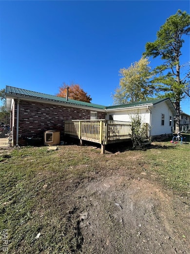 Back of property featuring a deck, brick siding, a metal roof, and a lawn