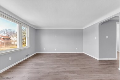 Unfurnished room with arched walkways, wood finished floors, baseboards, and visible vents