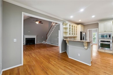 Kitchen featuring light hardwood / wood-style flooring, ceiling fan, a breakfast bar area, appliances with stainless steel finishes, and a high end fireplace