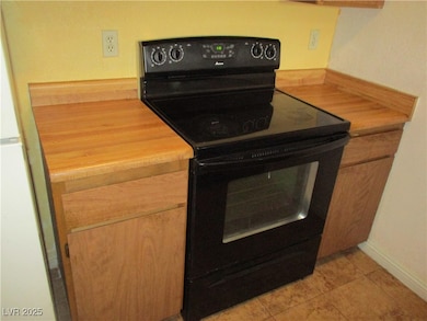 Kitchen featuring black range with electric cooktop, light countertops, light tile patterned flooring, and freestanding refrigerator
