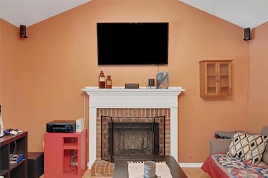 Living area featuring a brick fireplace, wood finished floors, lofted ceiling