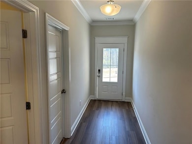 Doorway with dark wood-style floors, crown molding