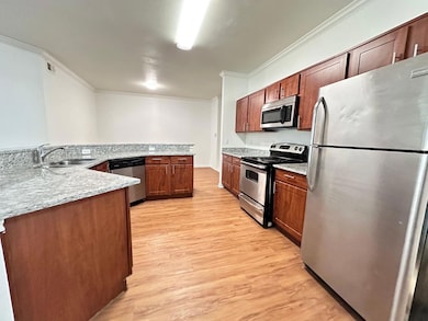 Kitchen featuring stainless steel appliances, light wood-type flooring, light stone countertops, and crown molding