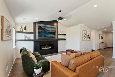Living area featuring a ceiling fan, wood finished floors, lofted ceiling, a glass covered fireplace, and recessed lighting