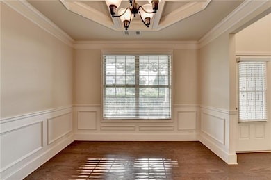 Spare room featuring a chandelier, dark wood finished floors, wainscoting, and ornamental molding