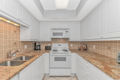 Kitchen with white appliances, light stone countertops, light tile patterned flooring, and tasteful backsplash