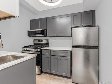 Kitchen with stainless steel appliances, gray cabinets, light wood-style flooring, and light stone countertops