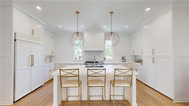 Kitchen featuring built in fridge, light wood finished floors, decorative backsplash, light countertops, and an island with sink