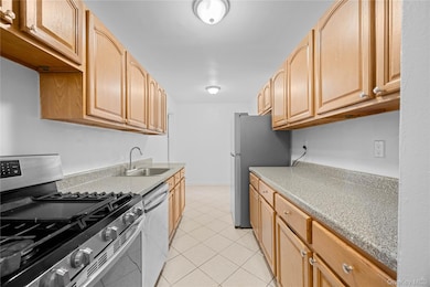 Kitchen with stainless steel appliances, light tile patterned flooring, light brown cabinets, and light stone countertops