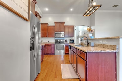 Kitchen with light stone countertops, appliances with stainless steel finishes, arched walkways, light wood-style floors, and ornamental molding