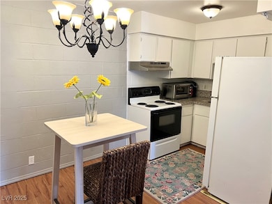 Kitchen with a toaster, under cabinet range hood, white appliances, white cabinets, and light wood-type flooring