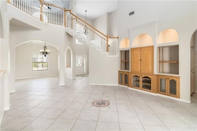 Unfurnished living room with a towering ceiling, a chandelier, light tile patterned floors, arched walkways, and built in shelves