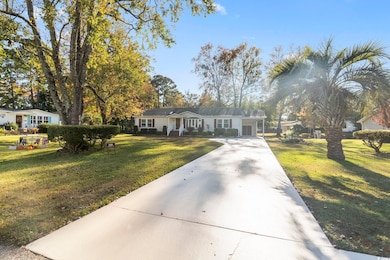 Ranch-style house featuring driveway, a front yard, covered porch, and a carport