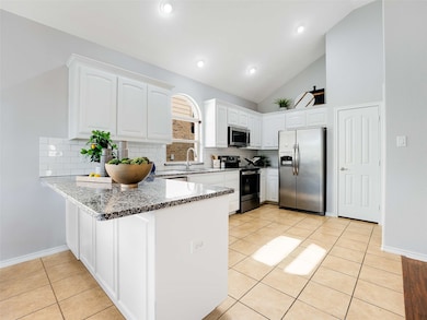 Kitchen featuring dark stone countertops, appliances with stainless steel finishes, white cabinets, light tile patterned floors, and a peninsula