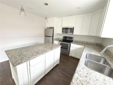 Kitchen with white cabinetry, appliances with stainless steel finishes, wood finish floors, pendant lighting, and a center island