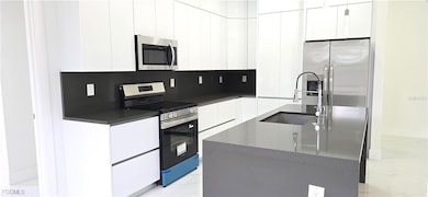 Kitchen featuring light marble finish floors, stainless steel appliances, modern cabinets, white cabinetry, and a center island with sink