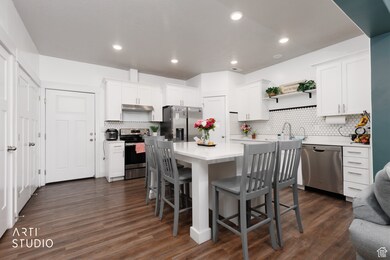 Kitchen featuring dark wood-type flooring, appliances with stainless steel finishes, a kitchen bar, a center island, and white cabinetry