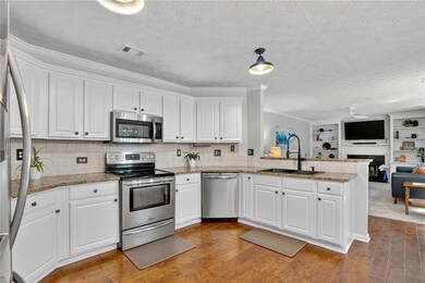 Kitchen with appliances with stainless steel finishes, light stone counters, white cabinetry, light wood finished floors, and crown molding