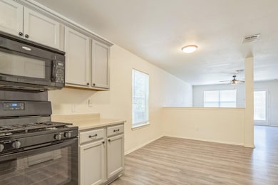 Kitchen featuring black appliances, plenty of natural light, light wood-type flooring, and light countertops
